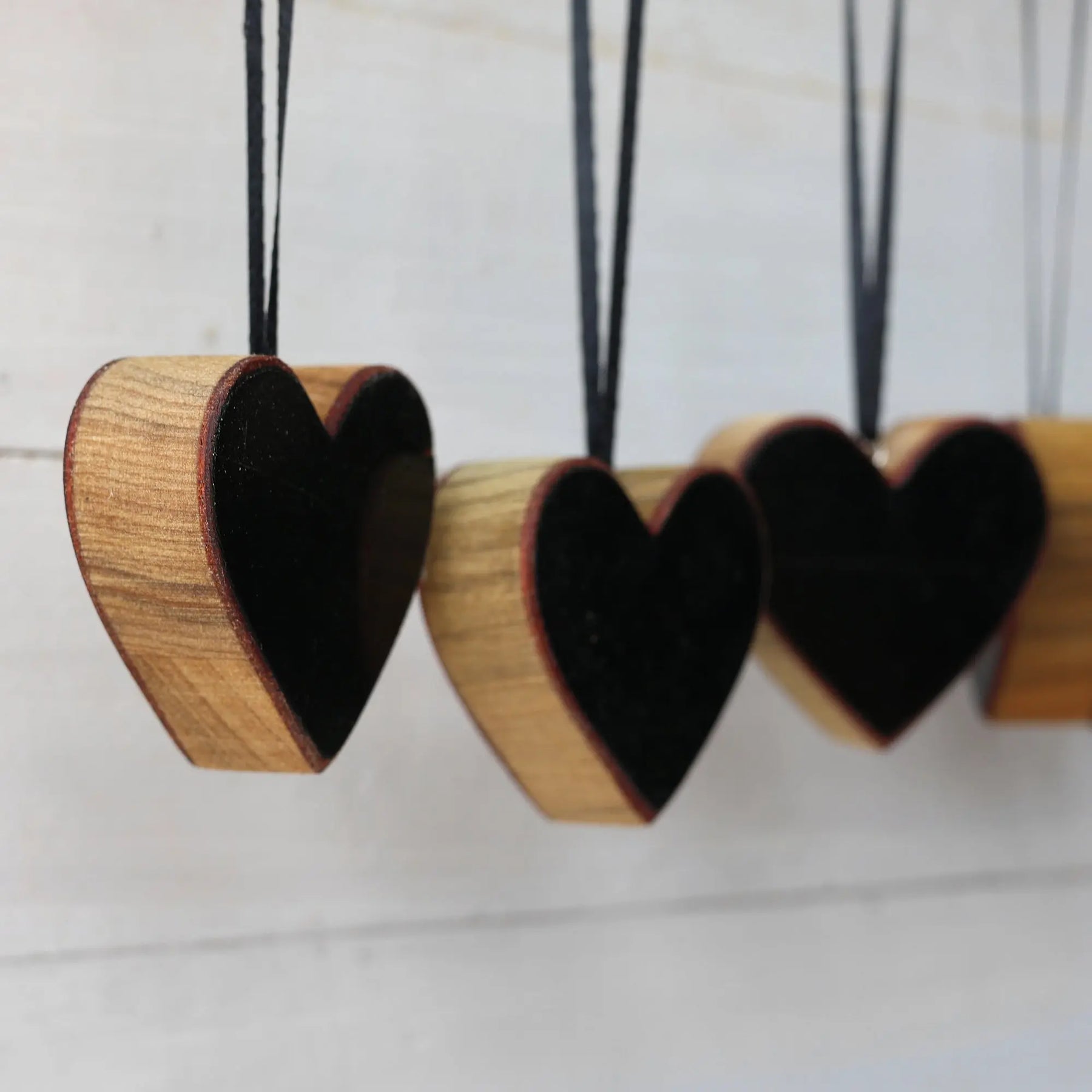 Wooden heart ornaments with black interiors hanging against a white background.
