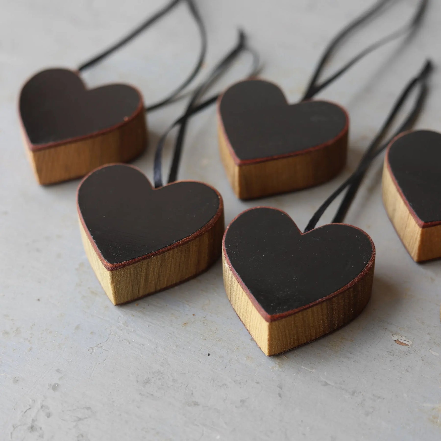 Wooden heart ornaments with black surfaces and black ribbon hangers.