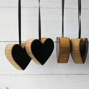 Wooden heart ornaments with black ribbon hangers against a white wood background.