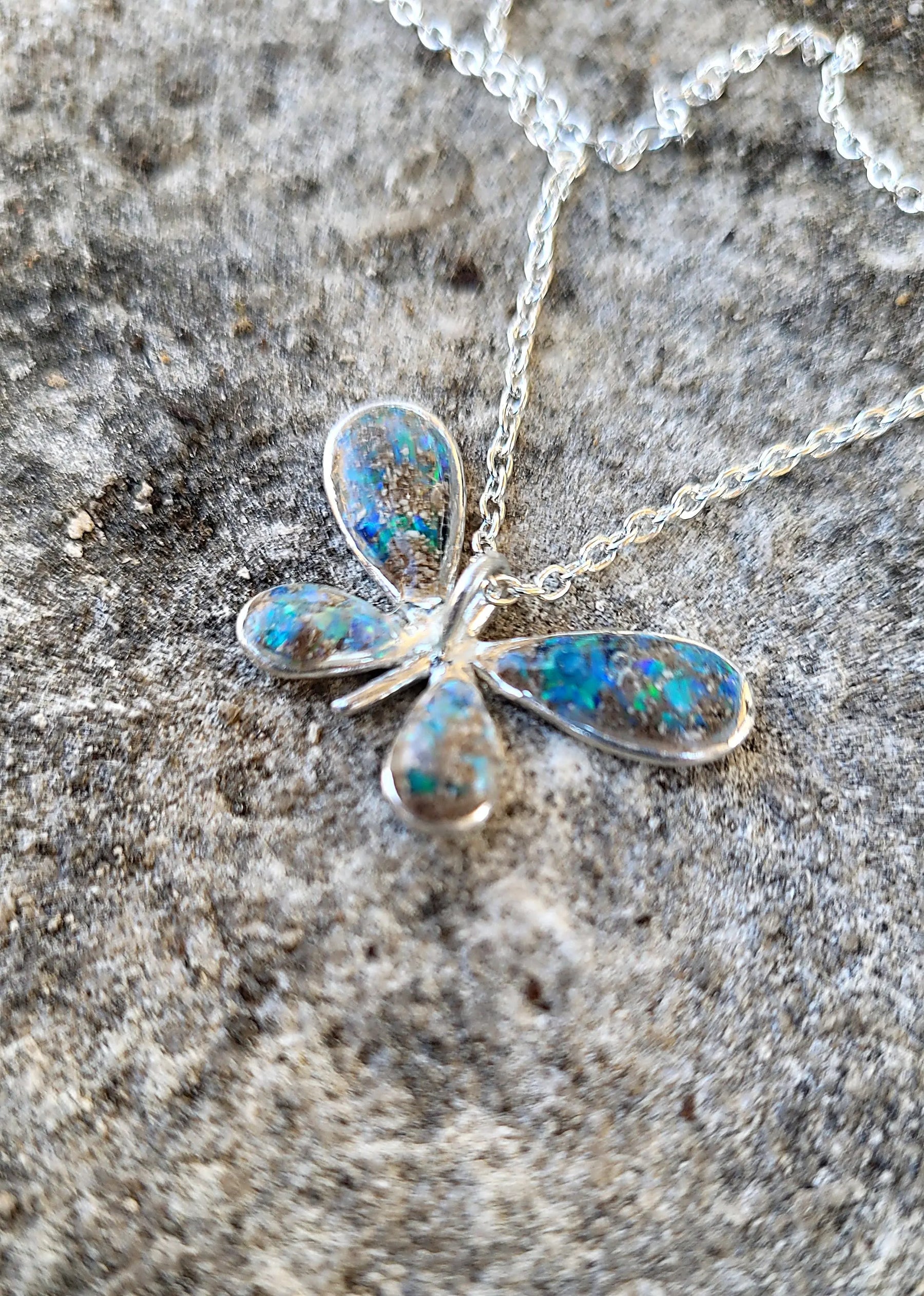 Sterling silver butterfly ash pendant with iridescent stone-like design on a chain, resting on a textured gray surface.