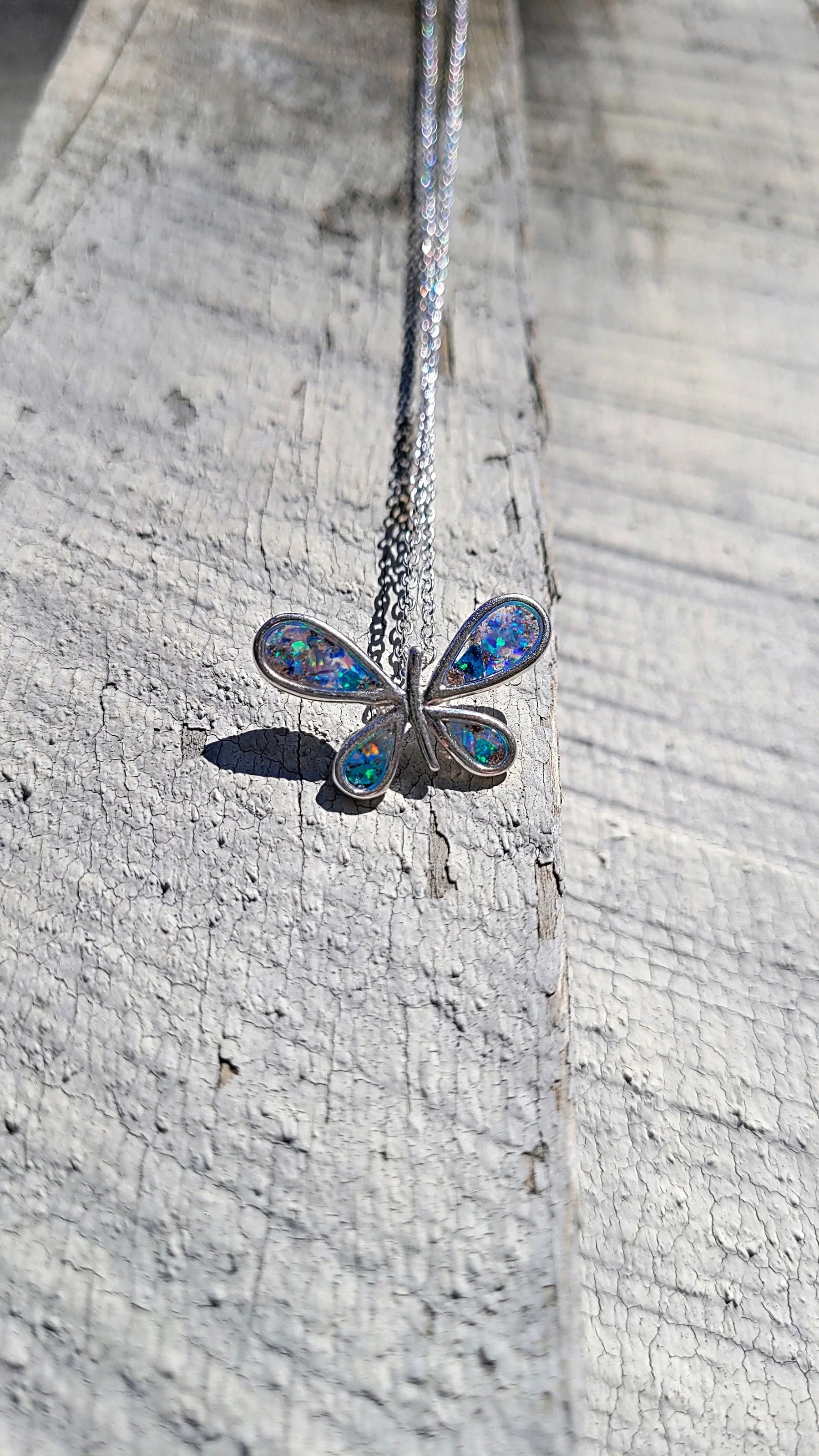 Sterling silver butterfly pendant with iridescent inlay on a textured wooden surface.
