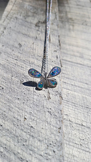Sterling silver butterfly pendant with iridescent inlay on a textured wooden surface.