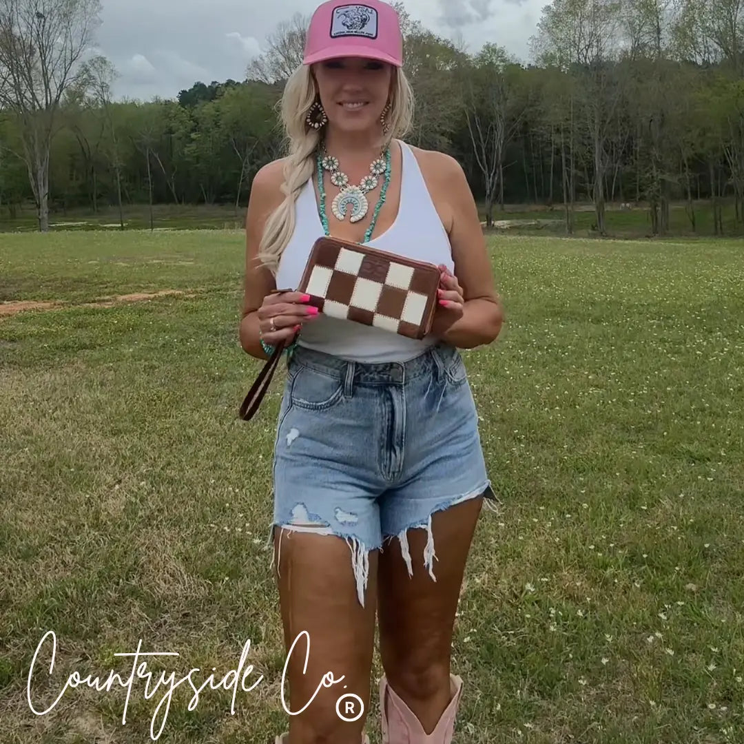 Brown and white checkered cowhide wallet with a wristlet held by a woman.