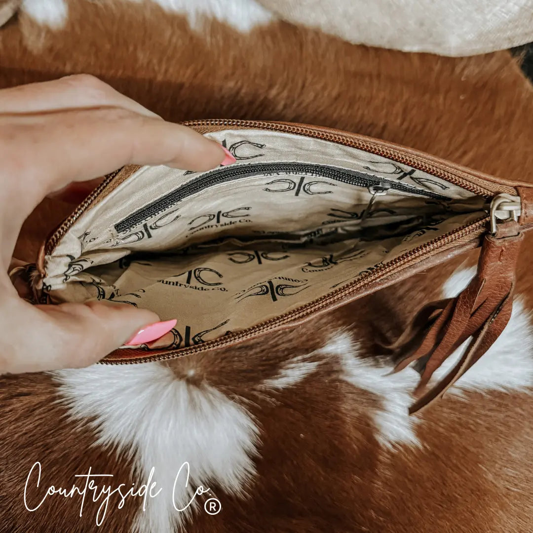 Brown leather wristlet pouch interior with Countryside Co. horseshoe lining and tassel.