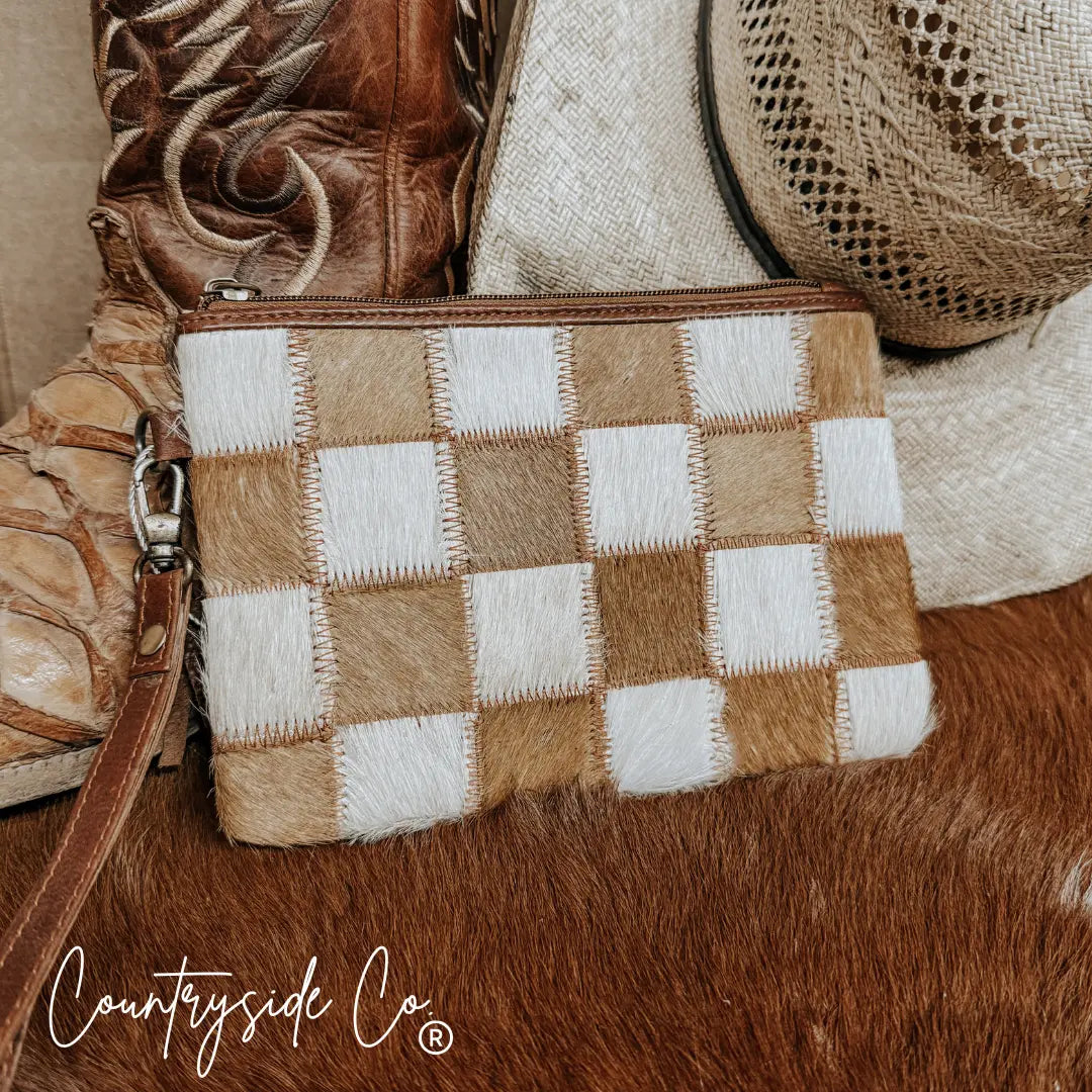 Checkered cowhide wristlet pouch with leather strap on a rustic background.