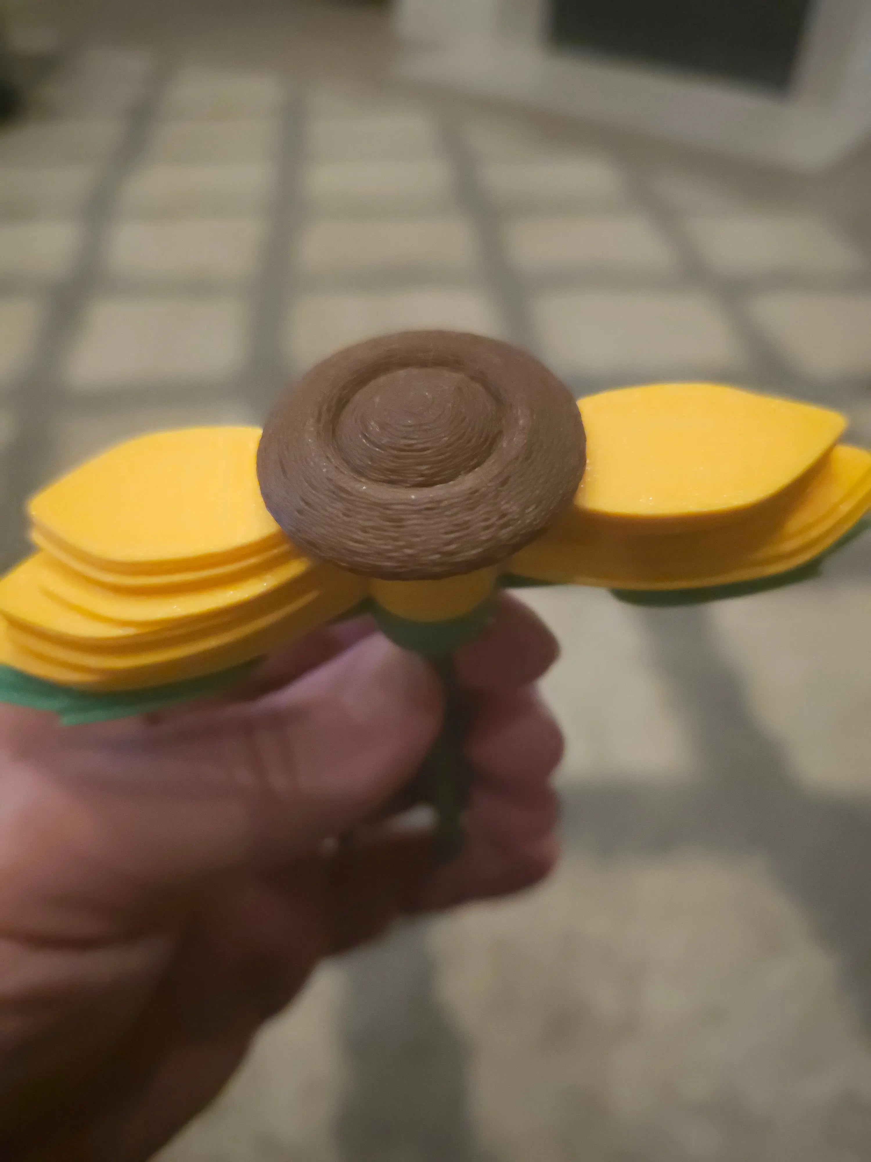3D Printed Sunflower Fidget Spinner: yellow petals, brown center, green stem. A sensory toy for focus and stress relief. Handheld spinner.