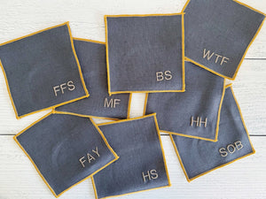 Grey linen coasters with yellow trim and embroidered letters like FFS, WTF, BS, MF, HH, FAY, HS, SOB.
