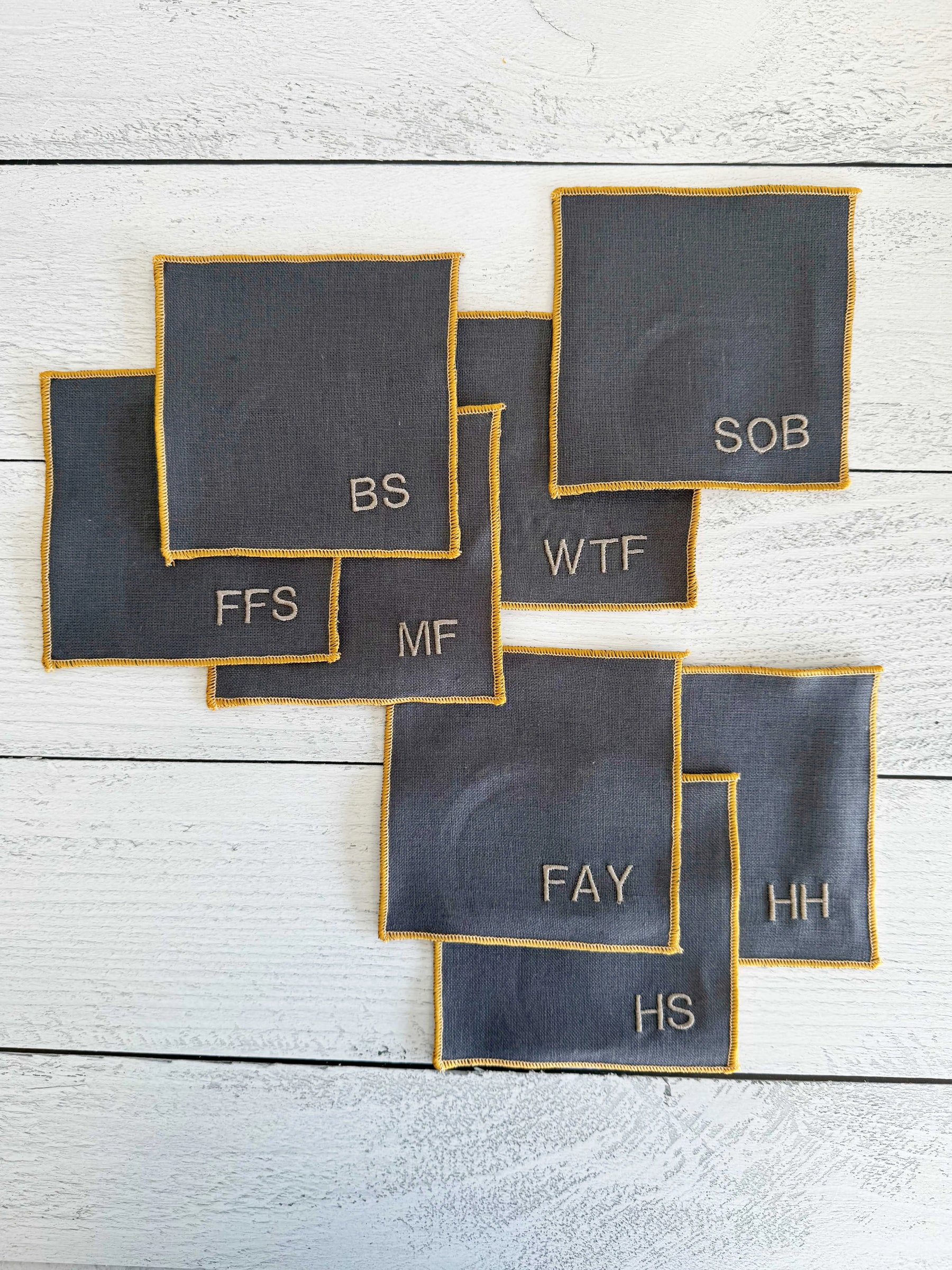 Grey linen coasters with embroidered monograms and yellow trim.