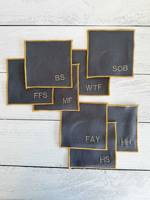 Grey linen coasters with embroidered monograms and yellow trim.