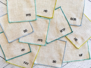 Set of 8 sweary cocktail coasters with embroidered letters on linen fabric.