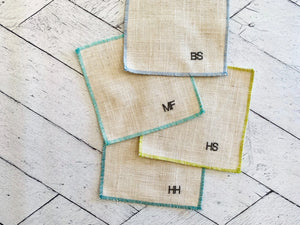 Linen cocktail coasters with monograms BS, MF, HS, and HH on a wooden background.