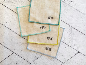 Set of 8 burlap cocktail coasters with embroidered letters on a white wooden surface