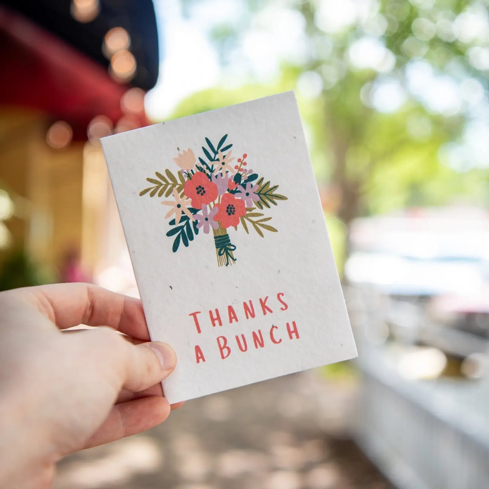 Plantable seed card with floral design and "Thanks a Bunch" text held by a hand.