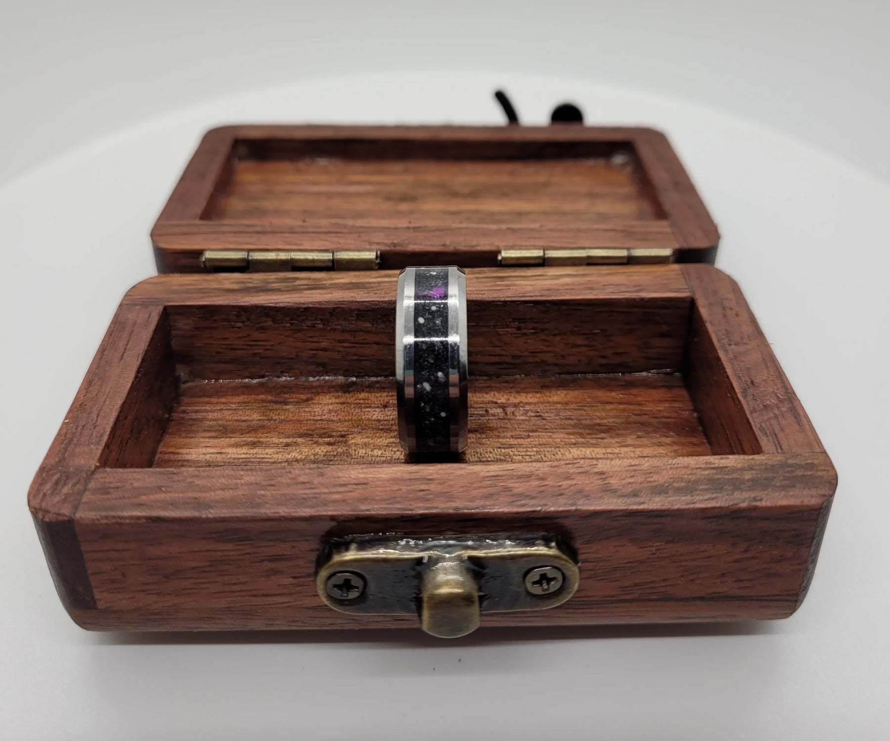 Memorial ring with ashes and constellation design inside a wooden box with a clasp on a white background.
