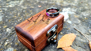 Constellation memorial ring on a wooden box engraved with names. The ring has ashes and purple glow elements.