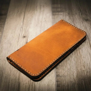 Brown leather long wallet with white stitching on a wooden surface.