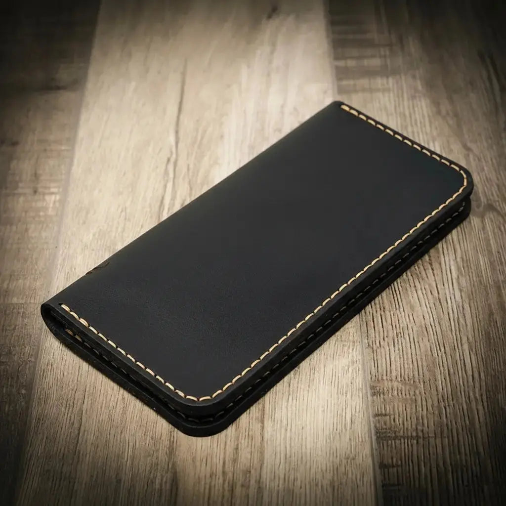 Black leather long wallet with tan stitching on a wooden background.