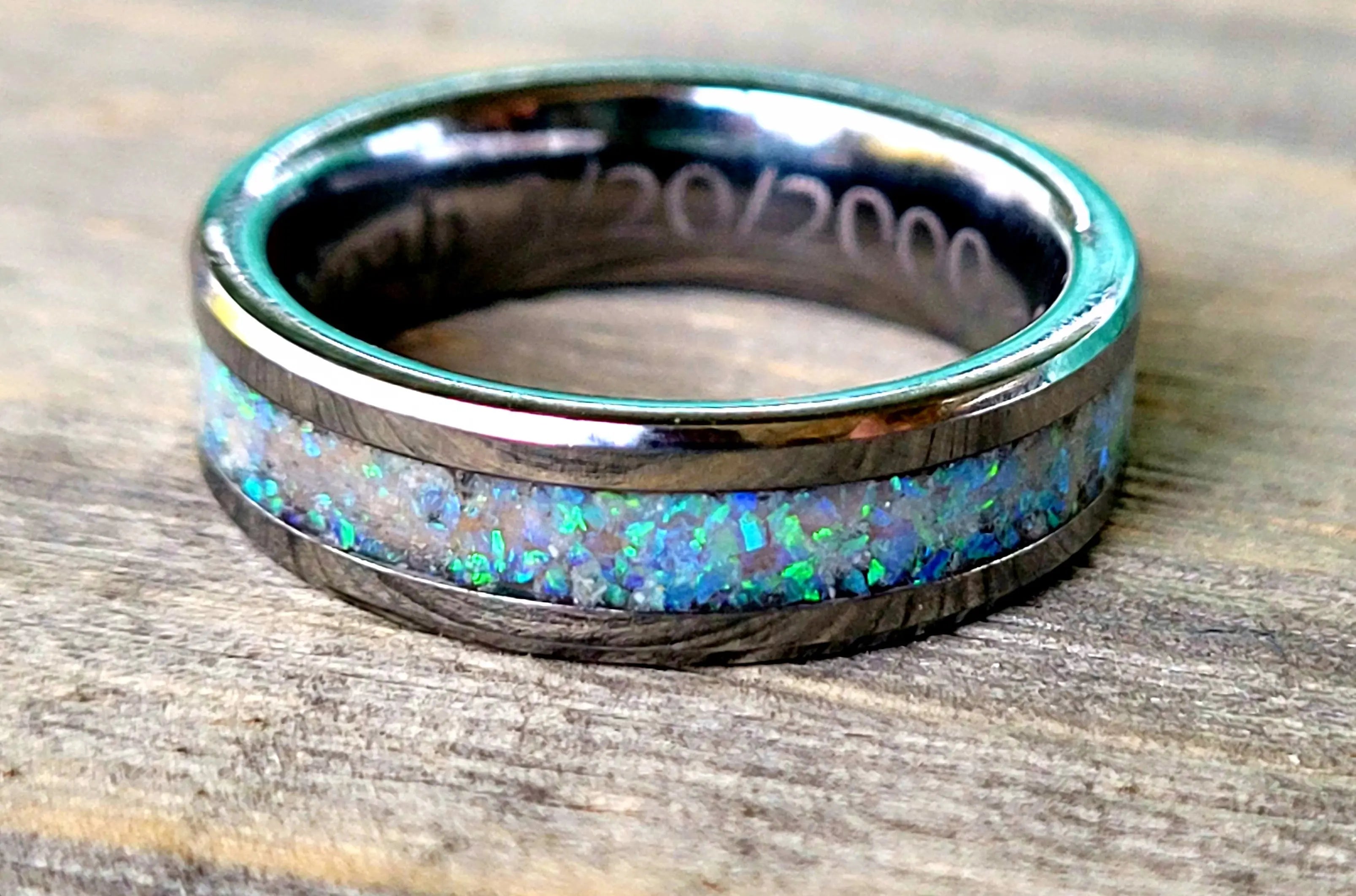 Memorial ring with blue opal inlay and inside engraving "20/20/2000" on a wood surface.