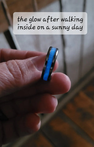Hand holding a black ring with a blue glowing center inlay.