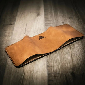 Brown leather trifold wallet with stitching and a dark logo on a wooden background.