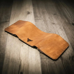 Brown leather trifold wallet with a bull logo on a wood background.