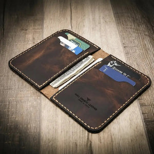 The Tyler vertical leather wallet holding cards and cash on a wooden surface.