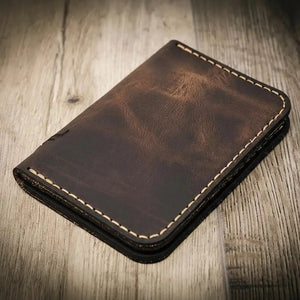 Dark brown leather vertical wallet with contrast stitching on a wooden surface.