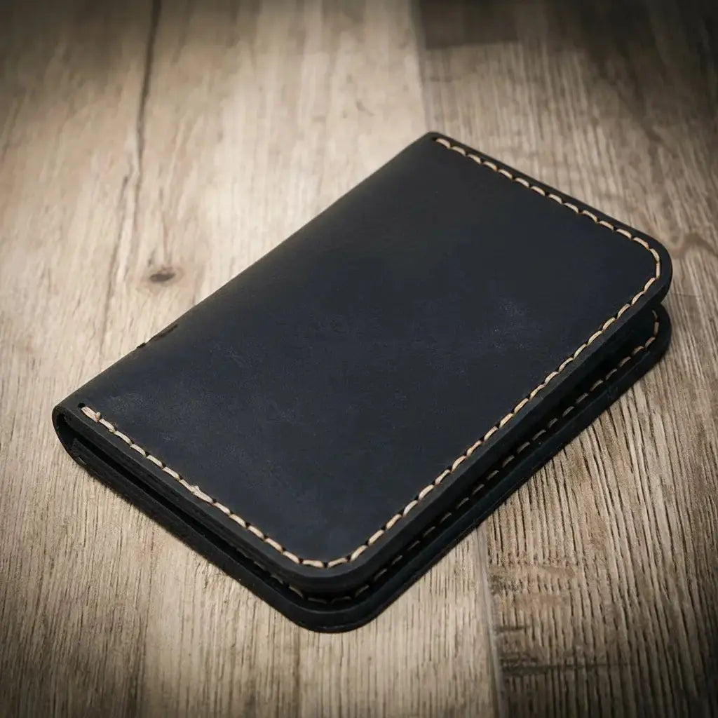 Black minimalist vertical leather wallet with tan stitching on a wooden background.