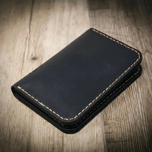 Black minimalist vertical leather wallet with tan stitching on a wooden background.