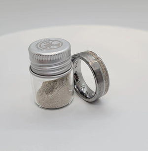 Memorial ring with ashes inlay next to a jar of ashes. Engraved message visible.