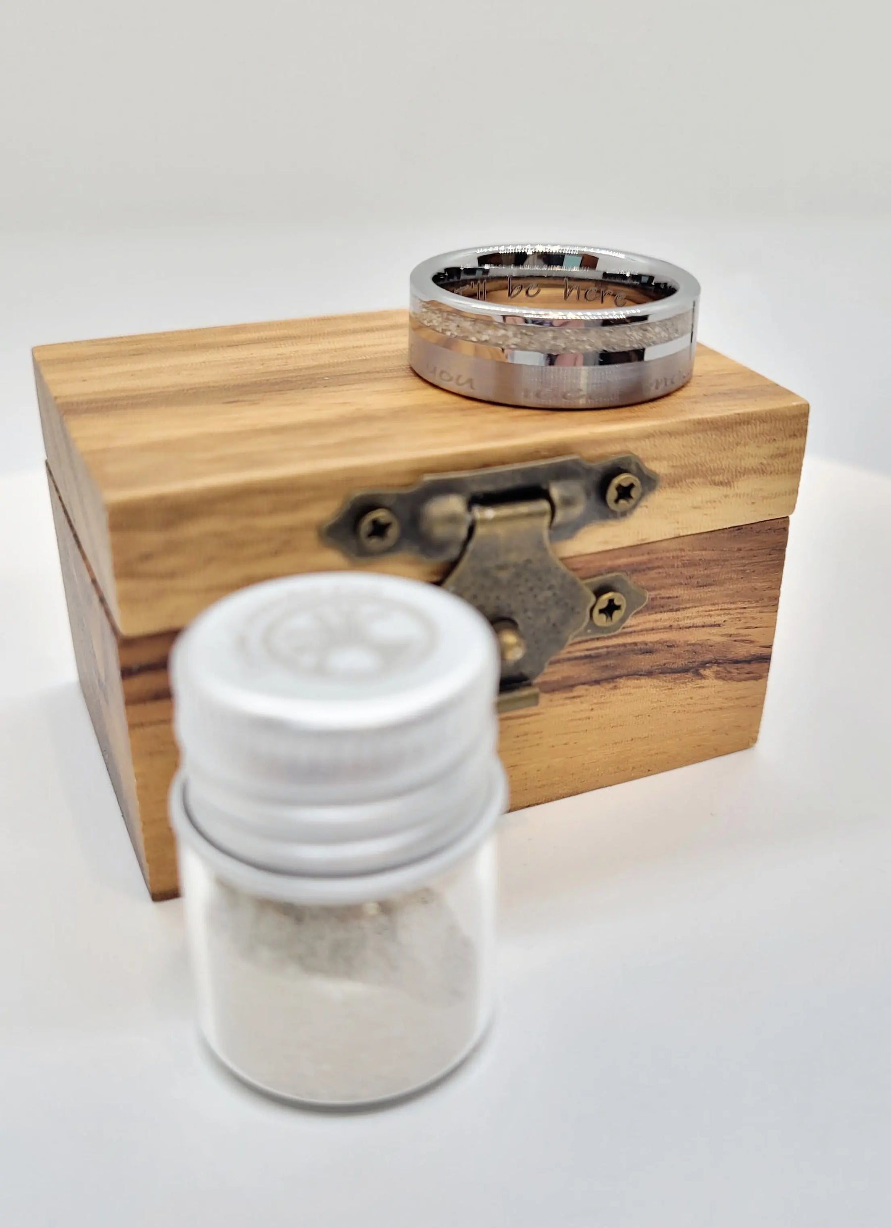 Memorial ring on wooden box with jar of ashes; tungsten ring, engraved, 8mm wide, with ashes inlay for remembrance.  