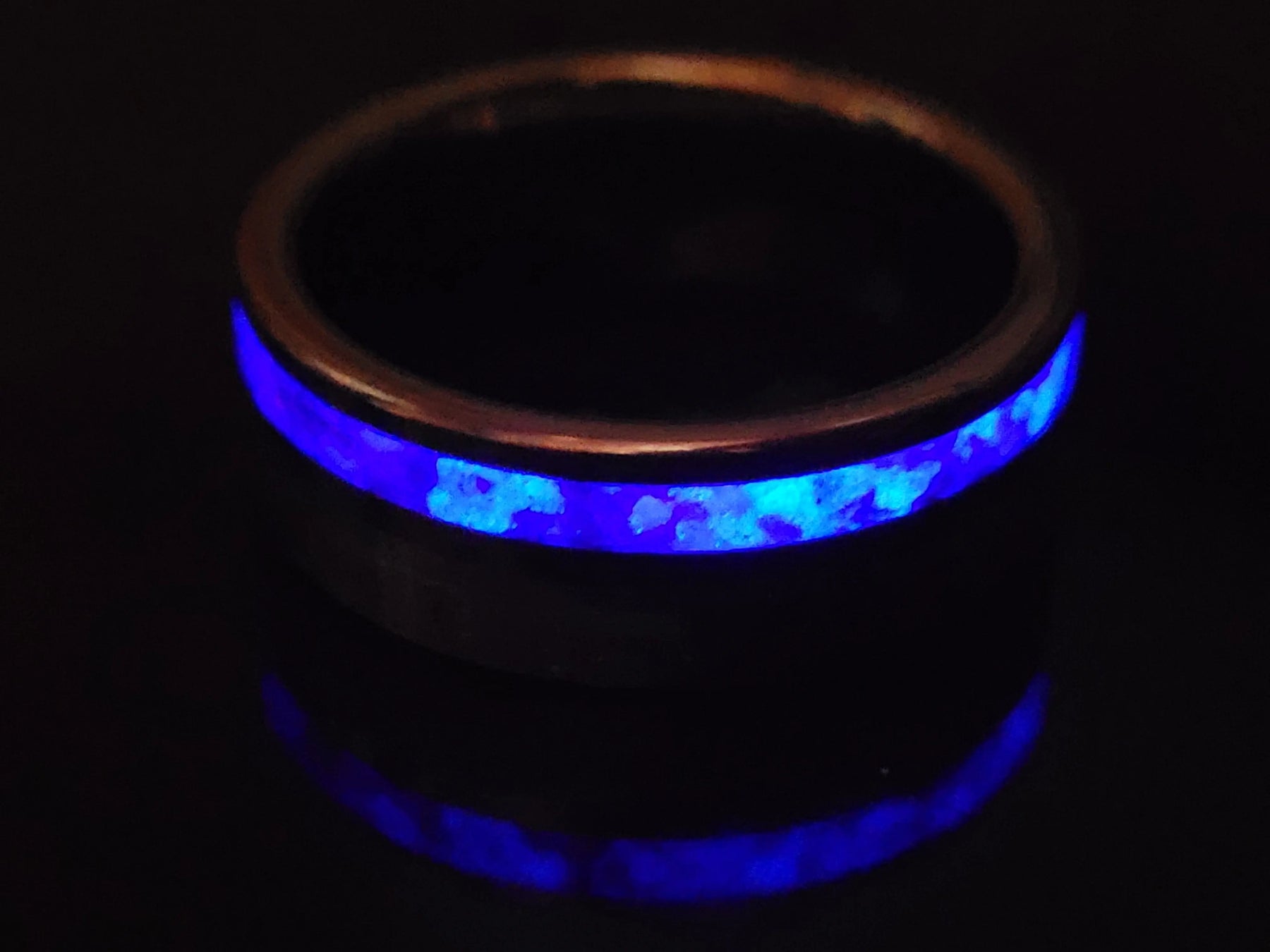 Tungsten ring with blue glow inlay and reflection in a dark setting.