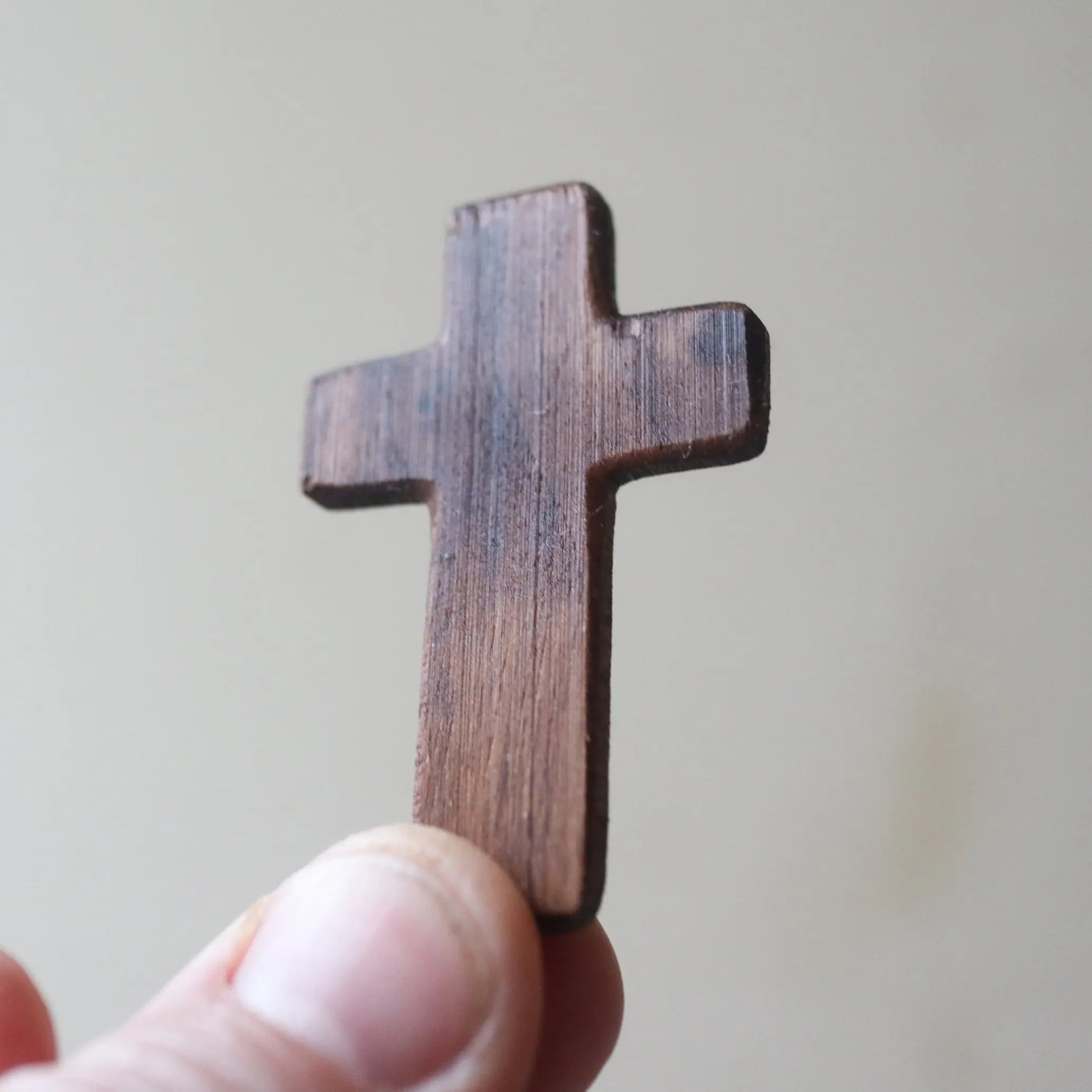 Wooden cross held between fingers against a light background.