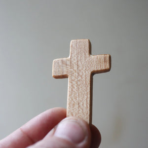 A person's hand holds a small wooden cross.