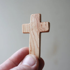 Wooden pocket cross held in a hand, showing natural wood grain.