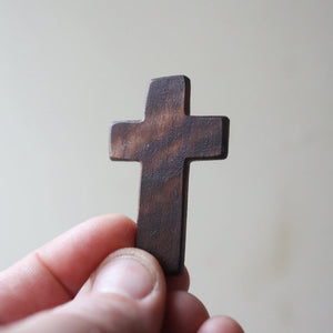 Hand holding a small, dark brown wooden cross.