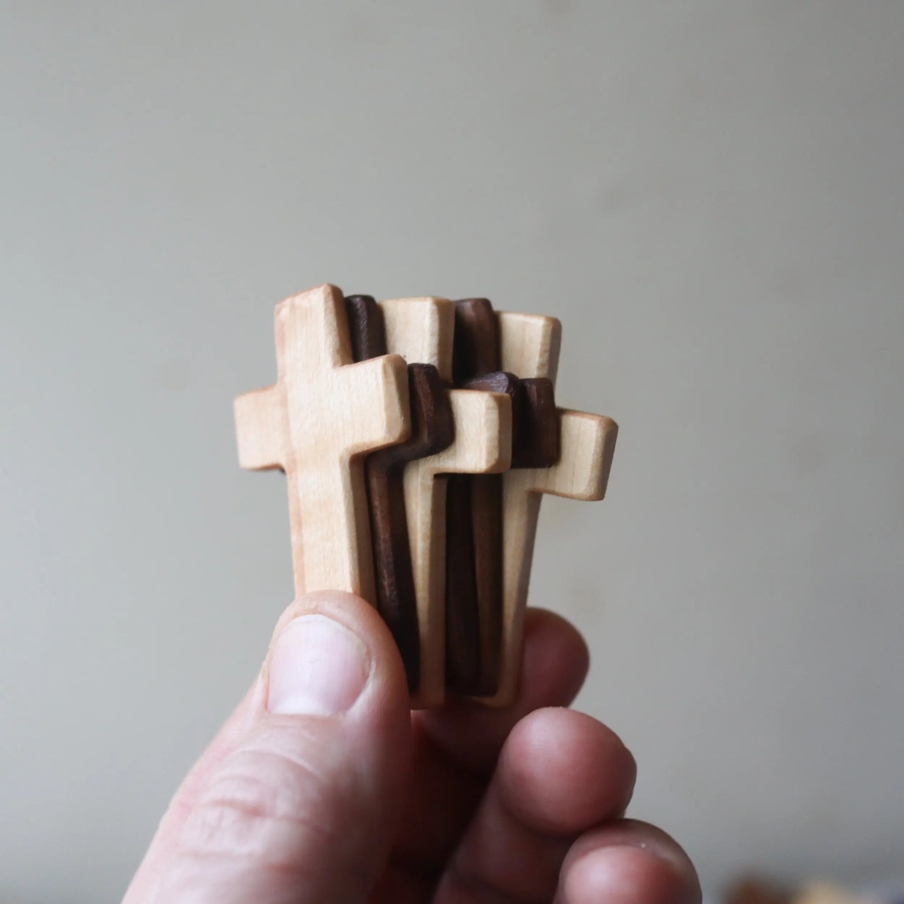 Hand holding stacked wooden crosses of light and dark wood.