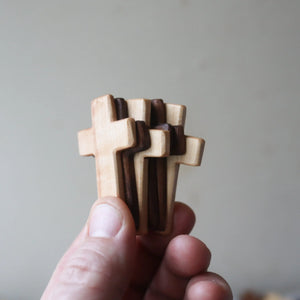 Hand holding stacked wooden crosses of light and dark wood.