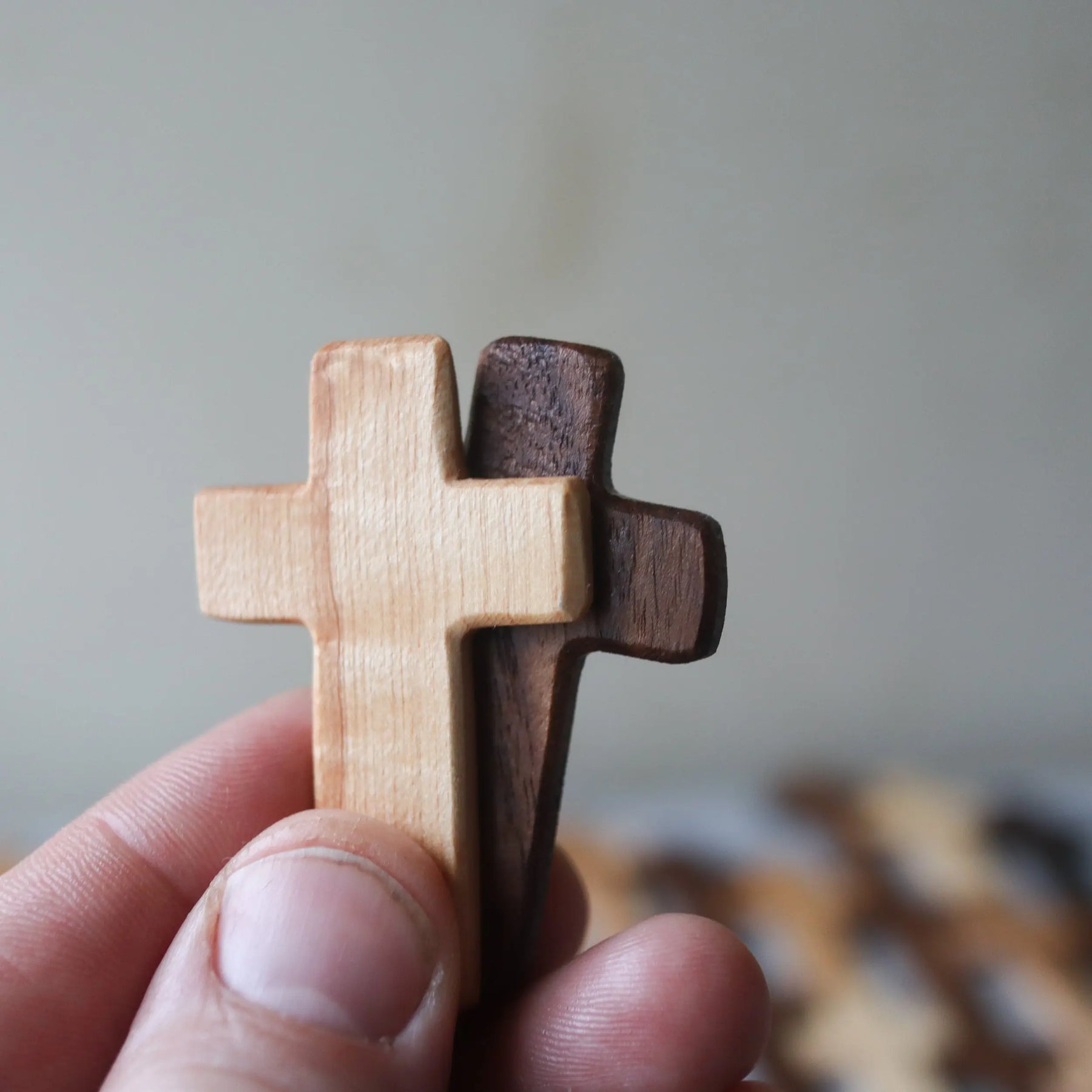 Two wooden crosses, one light and one dark, held in a hand.