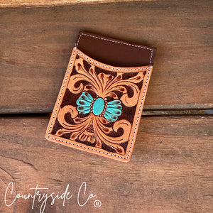 Brown tooled leather credit card holder with turquoise accent on a wooden surface.