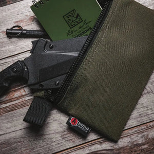 Green pouch with knife and Rite in the Rain notebook on a wooden surface