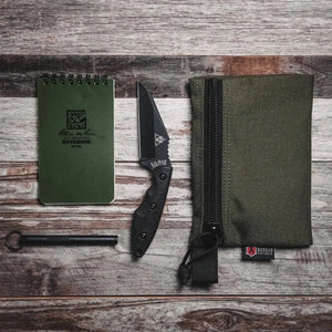 Olive green pouch, notebook, and knife on a wooden surface.