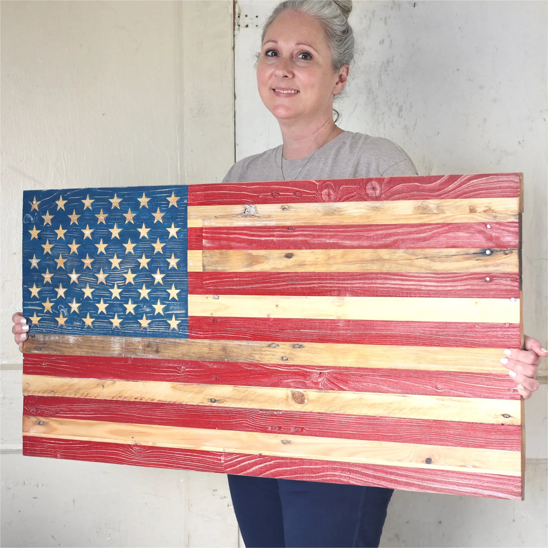 Woman holding a rustic handmade wooden American flag with hand-painted stars and stripes.