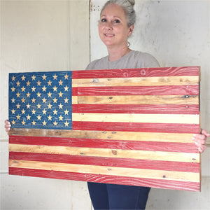 Woman holding a rustic handmade wooden American flag with hand-painted stars and stripes.