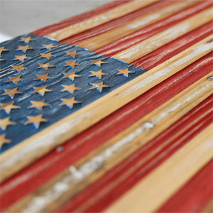 Close-up of a rustic wooden American flag with distressed red, white, and blue stripes and stars.