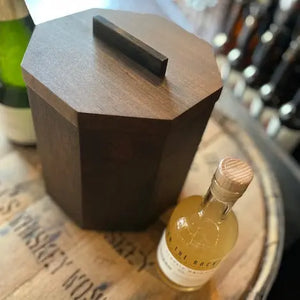 Octagonal cherry wood ice bucket with blackened steel handle on a wooden barrel.