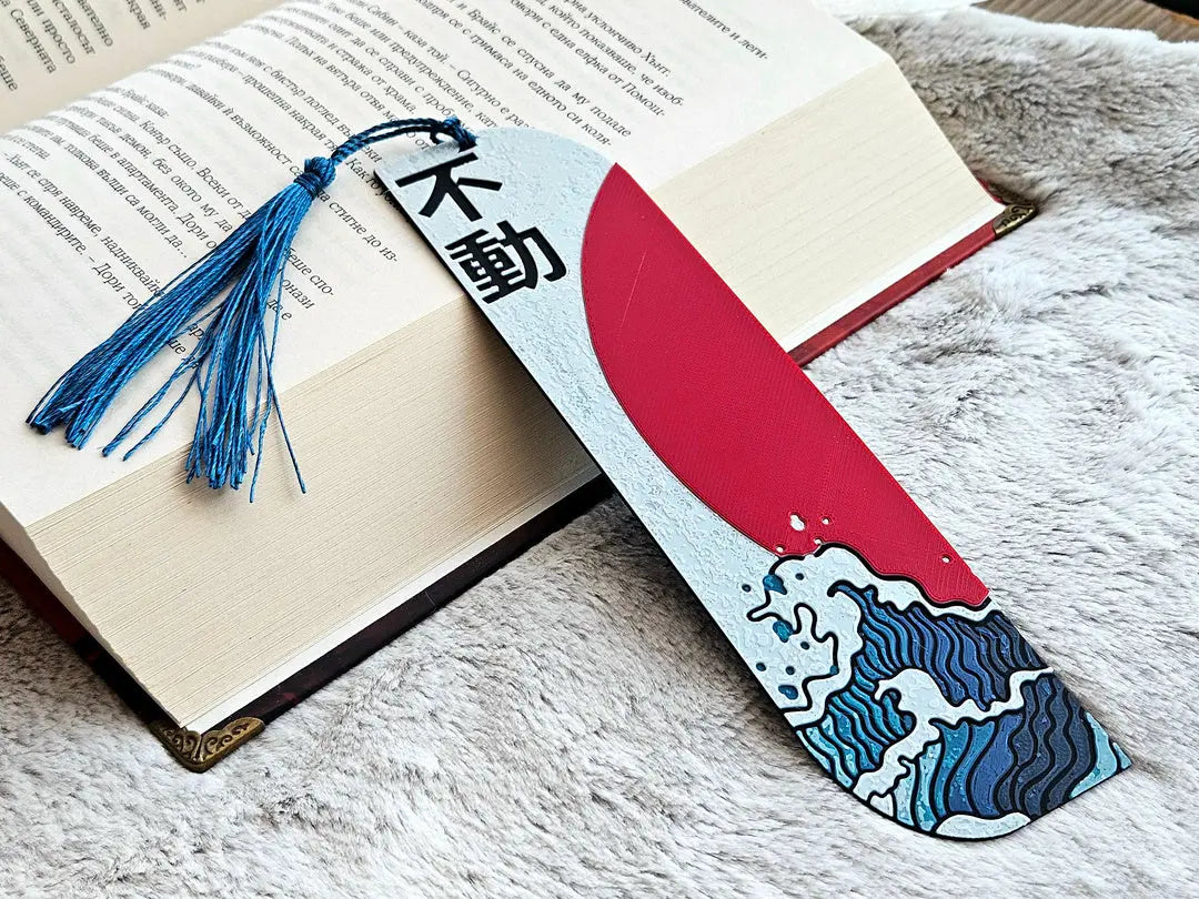 Japanese bookmark: ocean wave, red sun, and kanji 'unshakable' on a book with blue tassel.