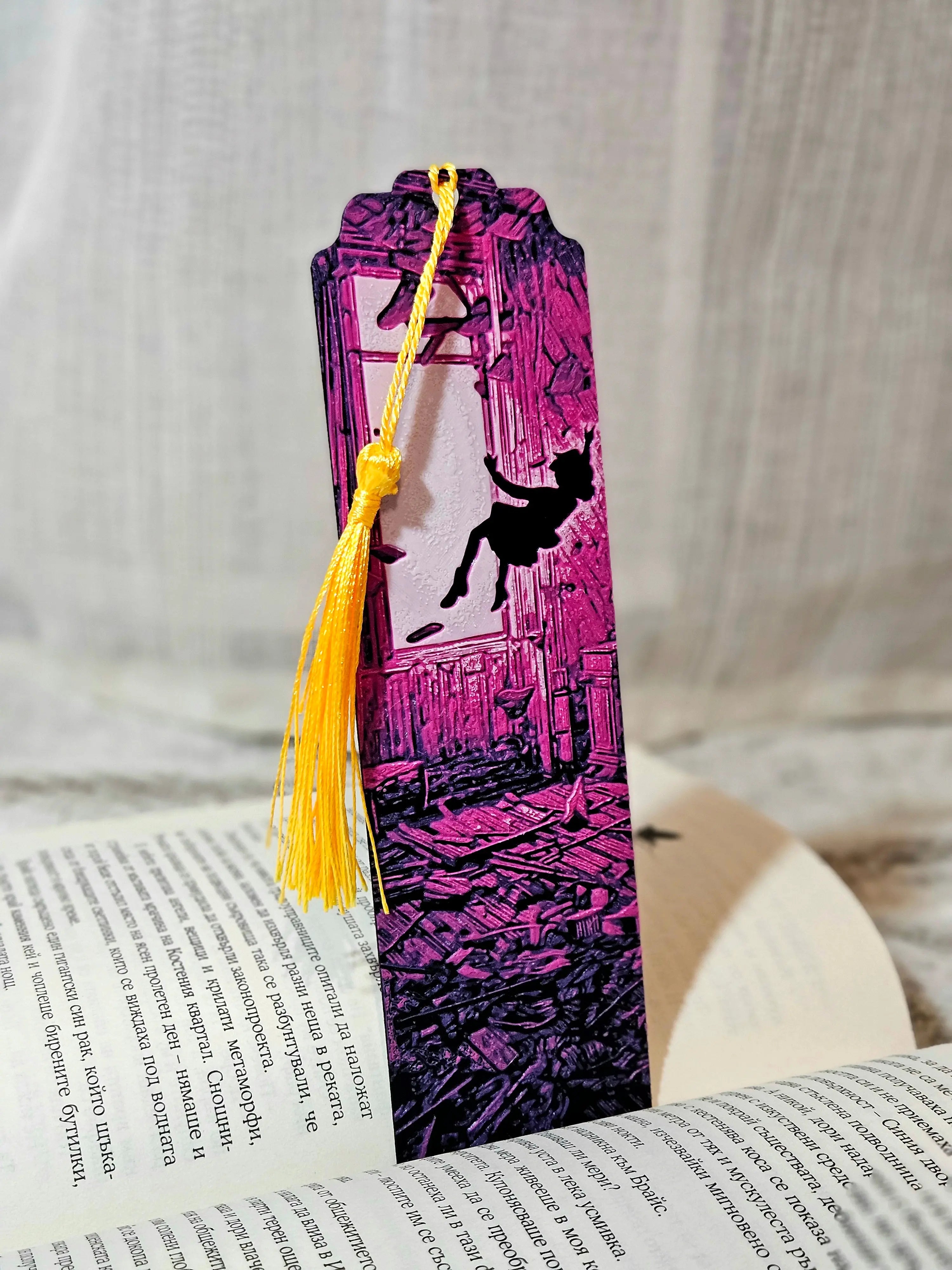 Purple 3D printed bookmark with a falling silhouette figure and yellow tassel on a book.