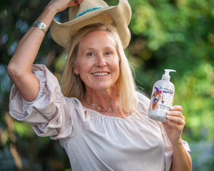 Woman in straw hat holding "The Appalachian Goat" Vanilla Goat's Milk Lotion bottle.
