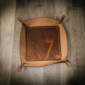 Brown leather valet tray with stitched edges on a wooden surface.